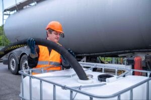 Worker handling industrial hose for H2S removal from oil storage tank in oil and gas processing facility.