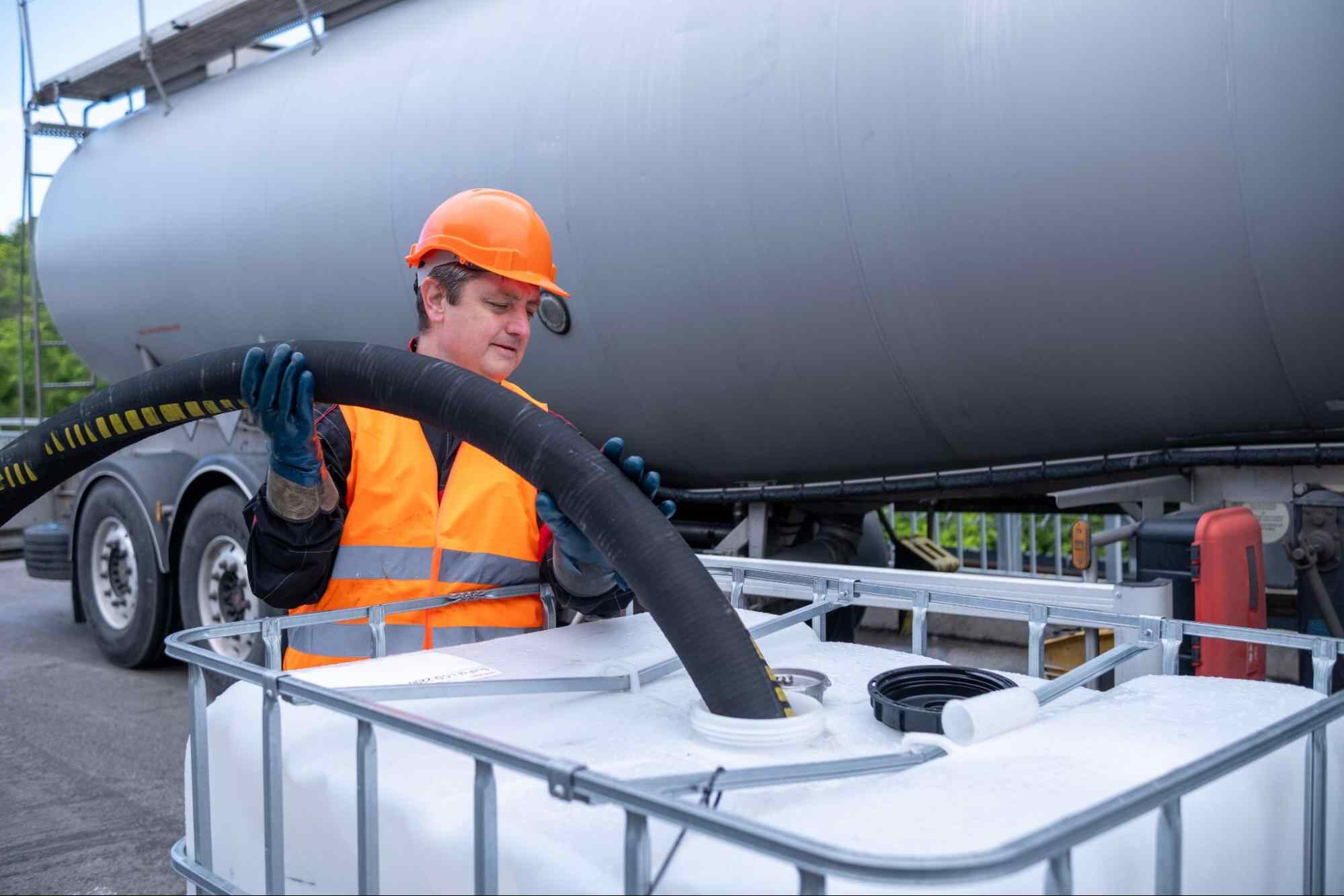 Worker handling industrial hose for H2S removal from oil storage tank in oil and gas processing facility.