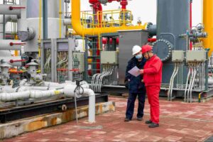 Industrial workers reviewing safety procedures at a processing plant with pipelines and equipment related to molten sulfur hazards and gas treatment operations.