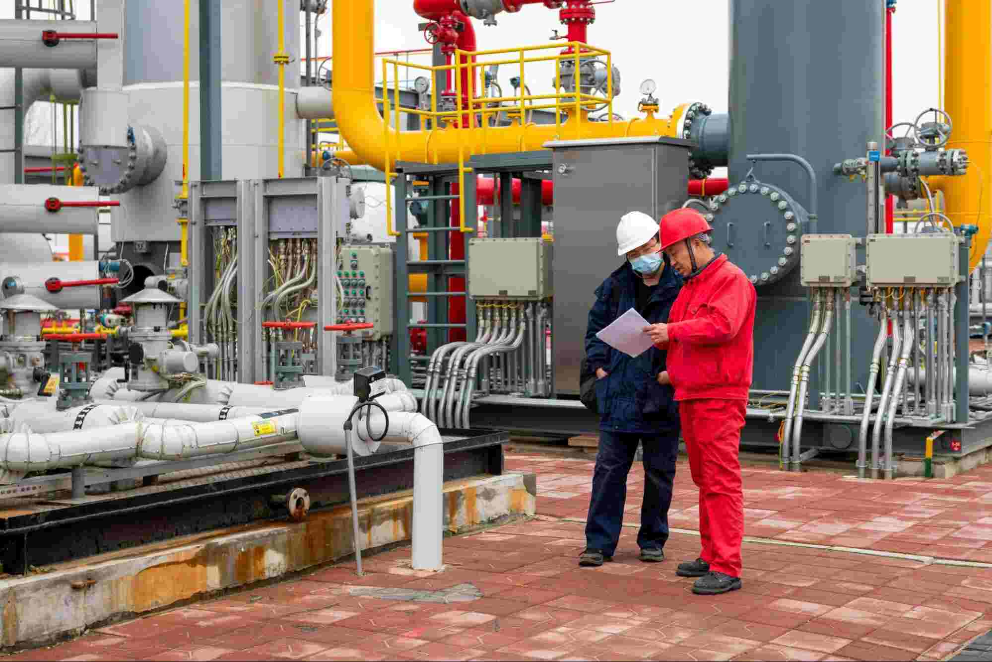 Industrial workers reviewing safety procedures at a processing plant with pipelines and equipment related to molten sulfur hazards and gas treatment operations.
