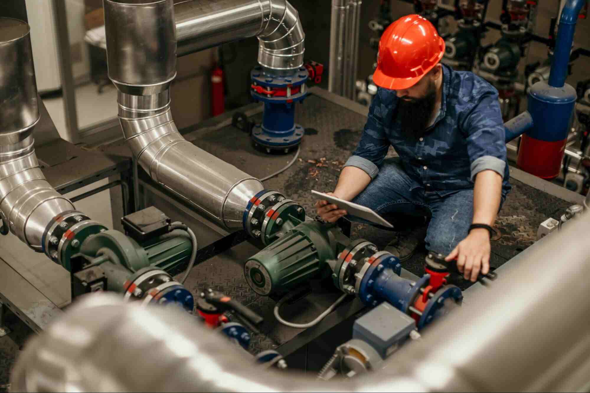 Technician inspecting industrial piping and pumps used for H₂S water treatment at an oil and gas processing facility.